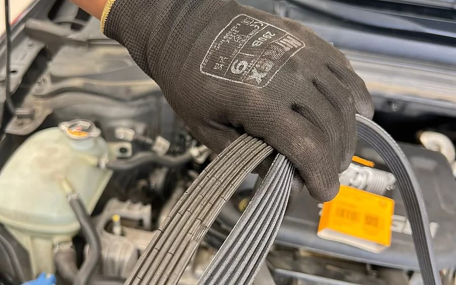Mano con guante ajustando la correa del motor de un coche en el taller.