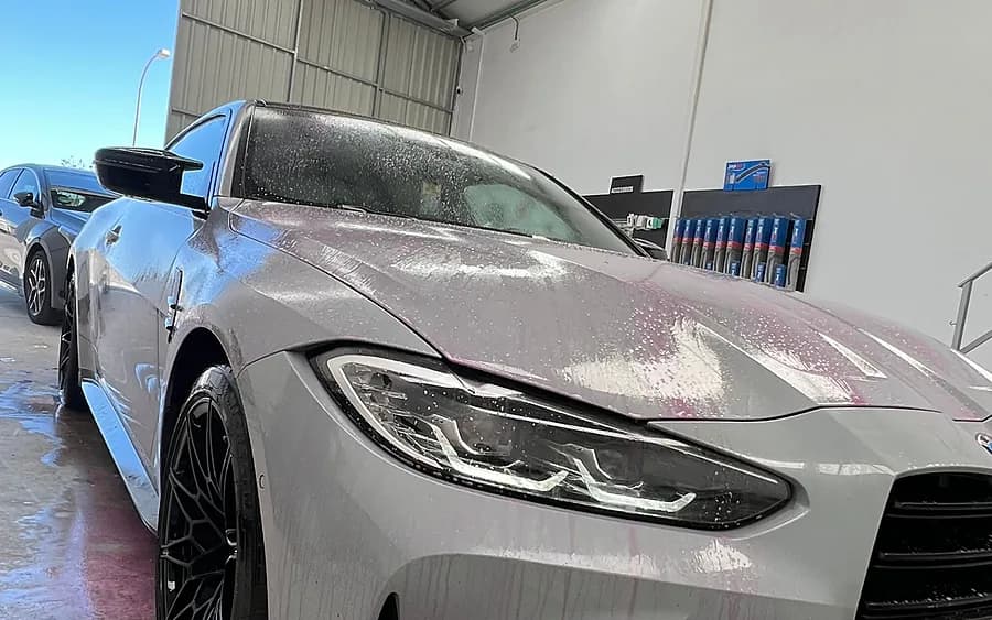 Espuma y agua sobre la carrocería de un coche durante el lavado exterior.