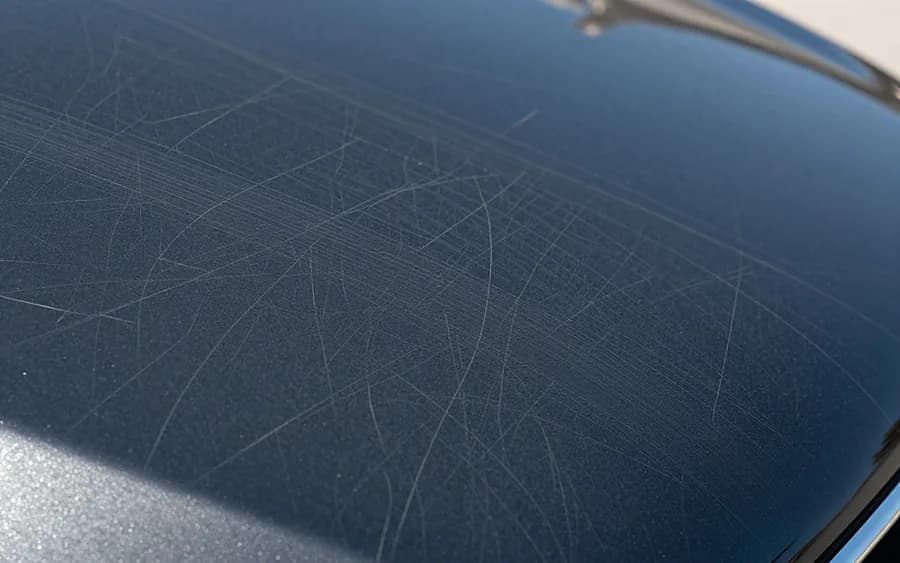 Detalle de arañazos sobre la pintura negra de la carrocería de un coche.