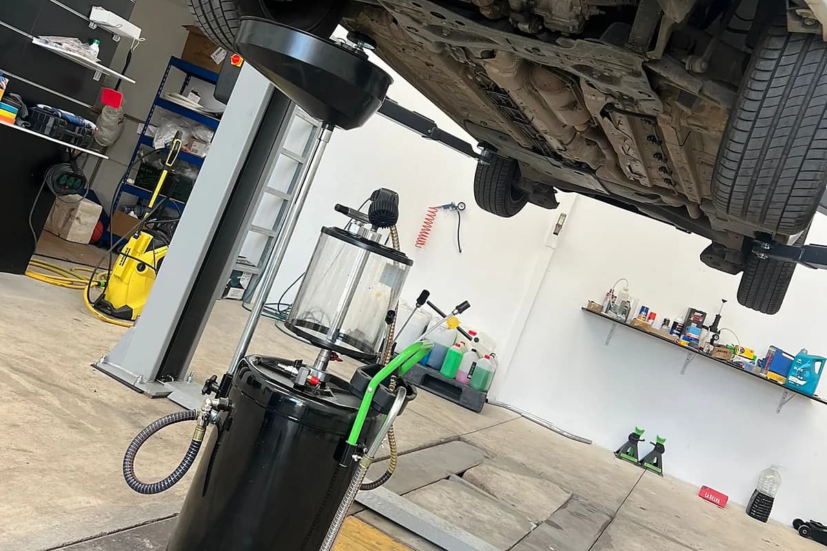 Extractor de aceite listo bajo un coche subido al elevador del taller.